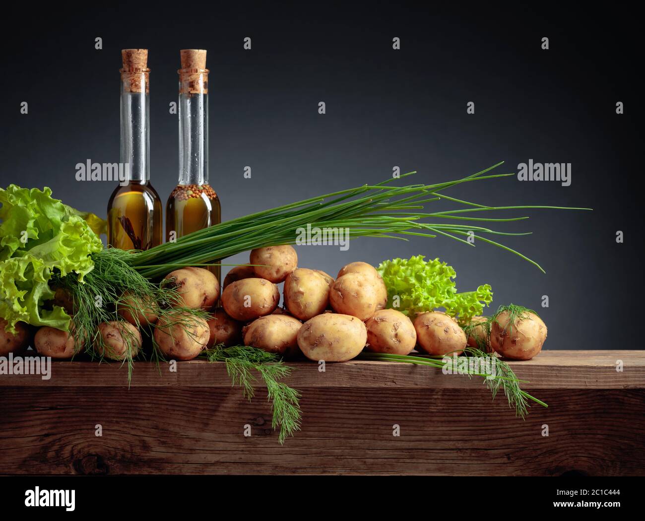 Young fresh organic potatoes with vegetable oil, dill, salad and onion on a old wooden table. Copy space. Stock Photo