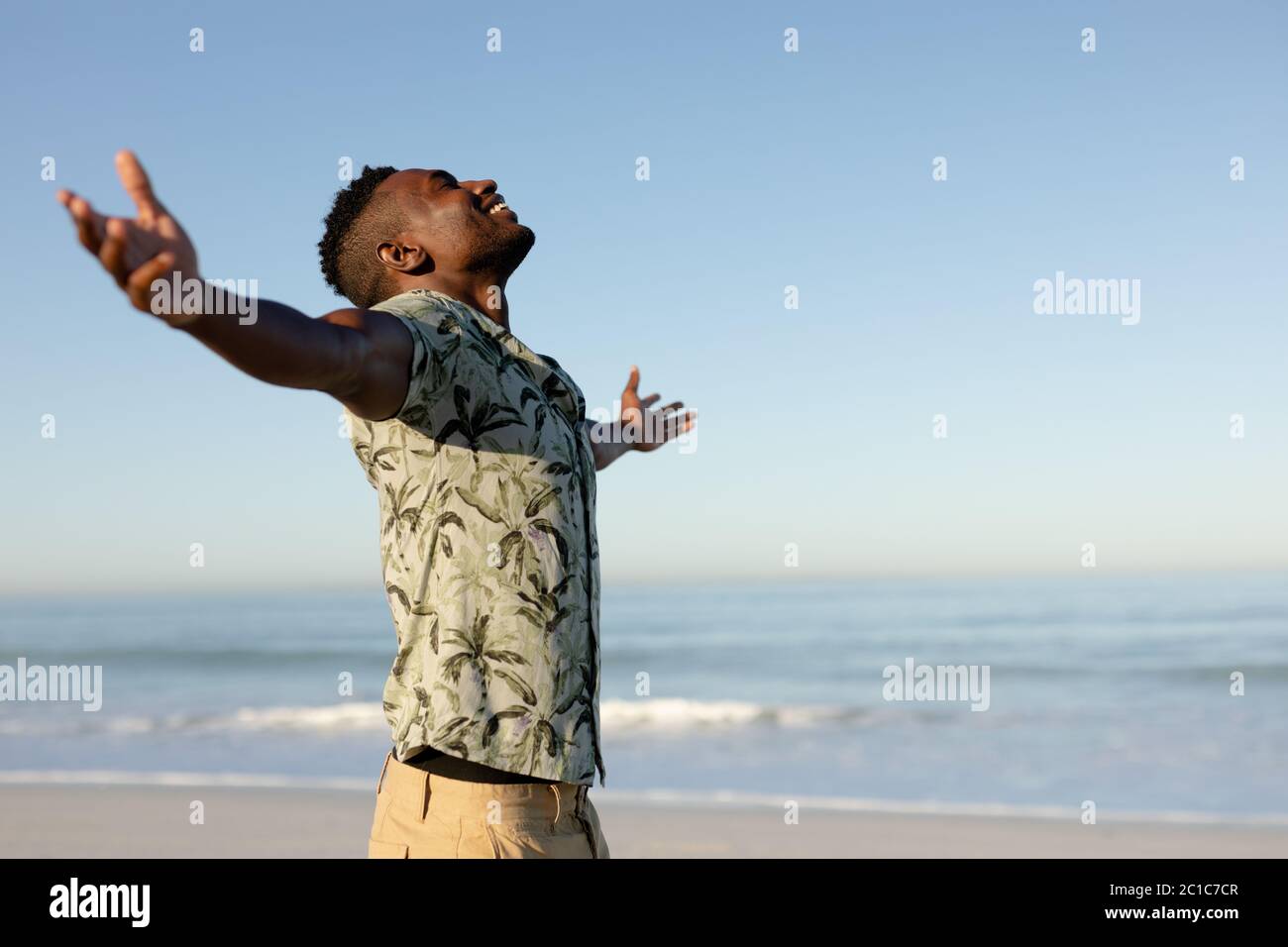 An African American man with his arms outstretched on beach on a sunny day Stock Photo