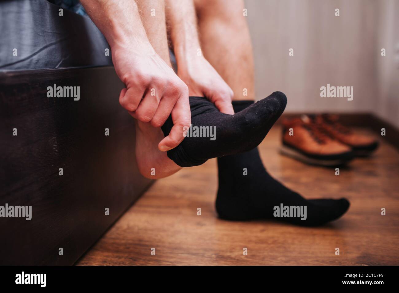 Close-up. A man puts a sock on the background of shoes. He is sitting on his bed. Stock Photo