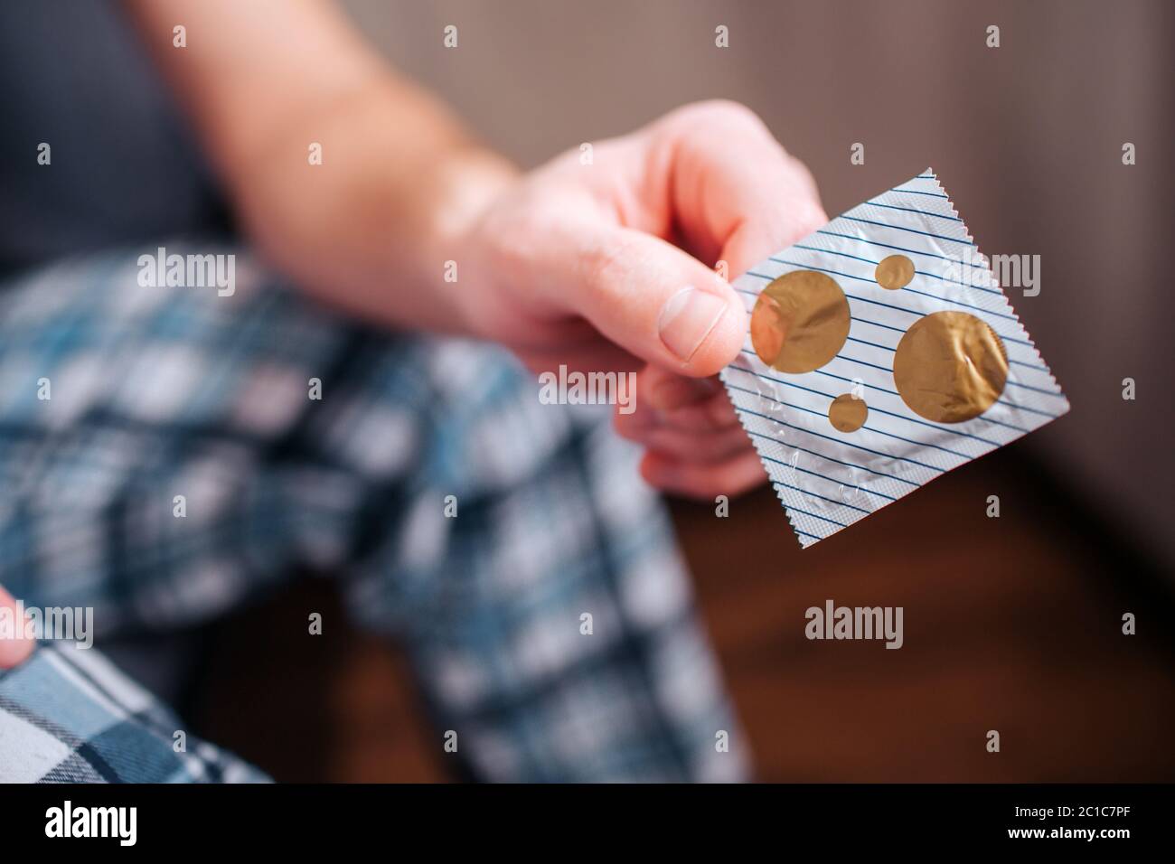 Close-up. A condom in the hands of a man. Against the background of the apartment and the bed. Stock Photo