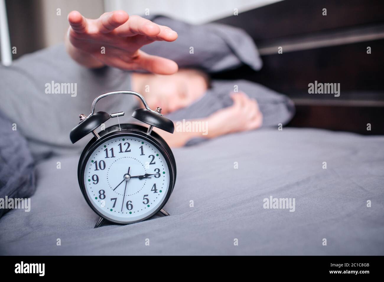 no strength to get out of bed in the morning. A man in the morning in the bed does not want to wake up. wants to turn off the alarm Stock Photo