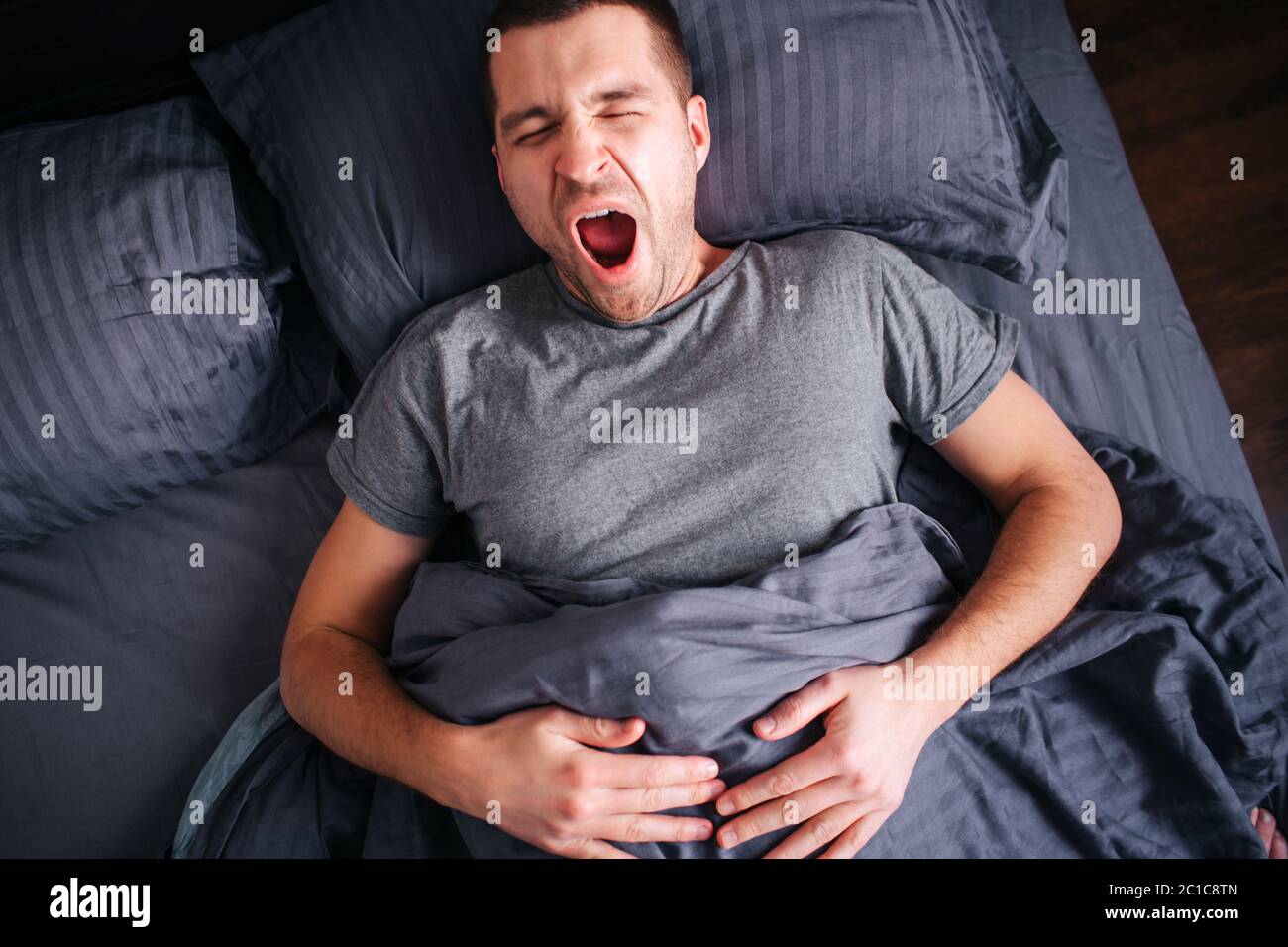 Sleepy man in the bed yawns. View from above. Male model wakes up early in the morning Stock Photo