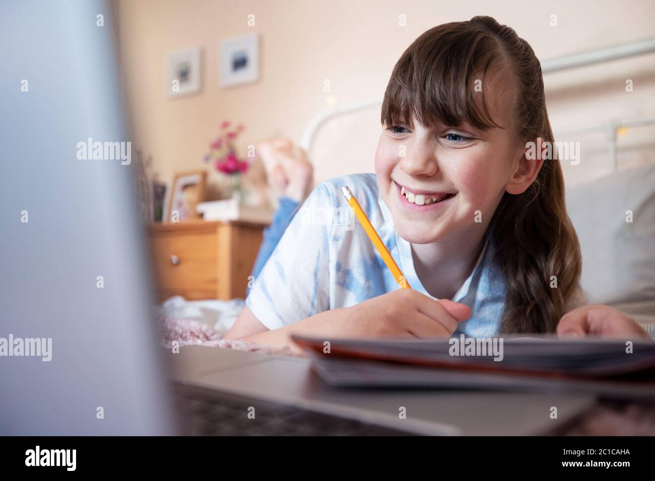 Young Girl Lying On Bed In Bedroom With Laptop Studying And Home