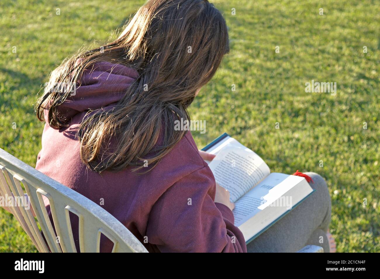 Young white female sitting in the sun reading a book. Unplugged from technology Stock Photo