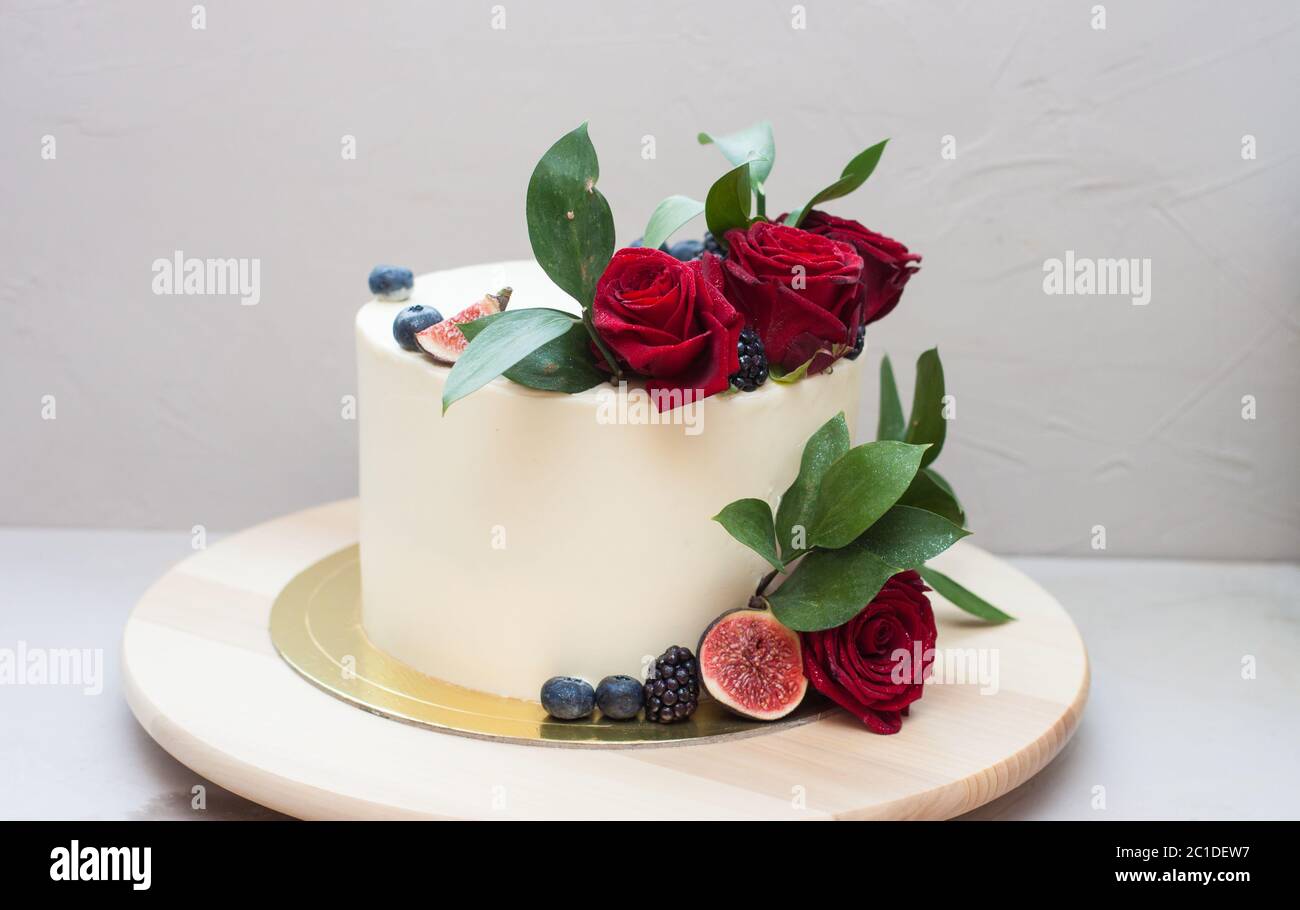 Elegant wedding cake decorated with fresh red roses, green leaves, figs and  blueberry. Plain grey background Stock Photo - Alamy