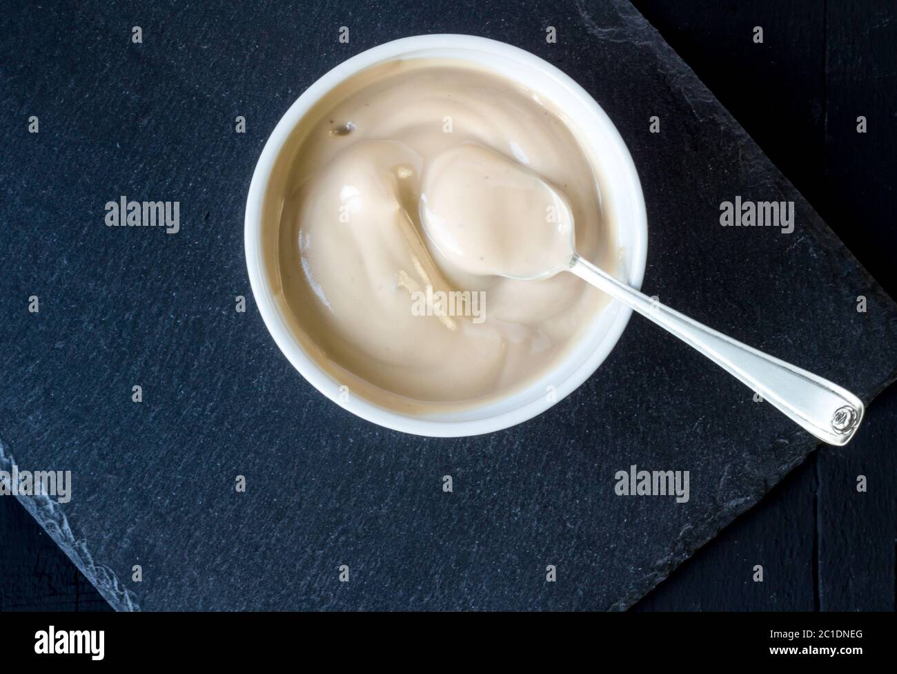 Yoghurt in white cup with silver spoon on rustic slate black background