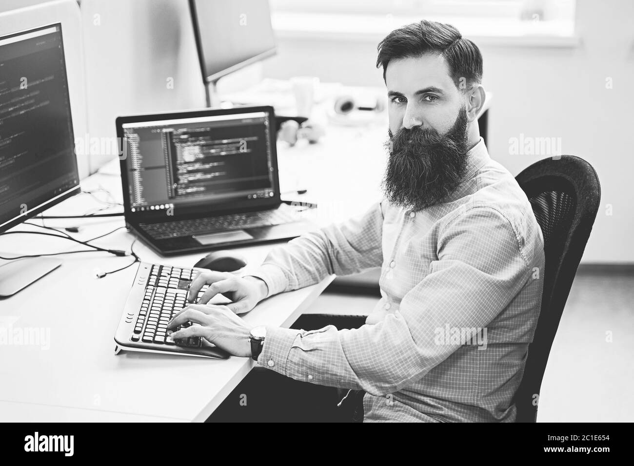 Serious computer programmer developer working in IT office, sitting at desk and coding, working on a project in software development company or Stock Photo