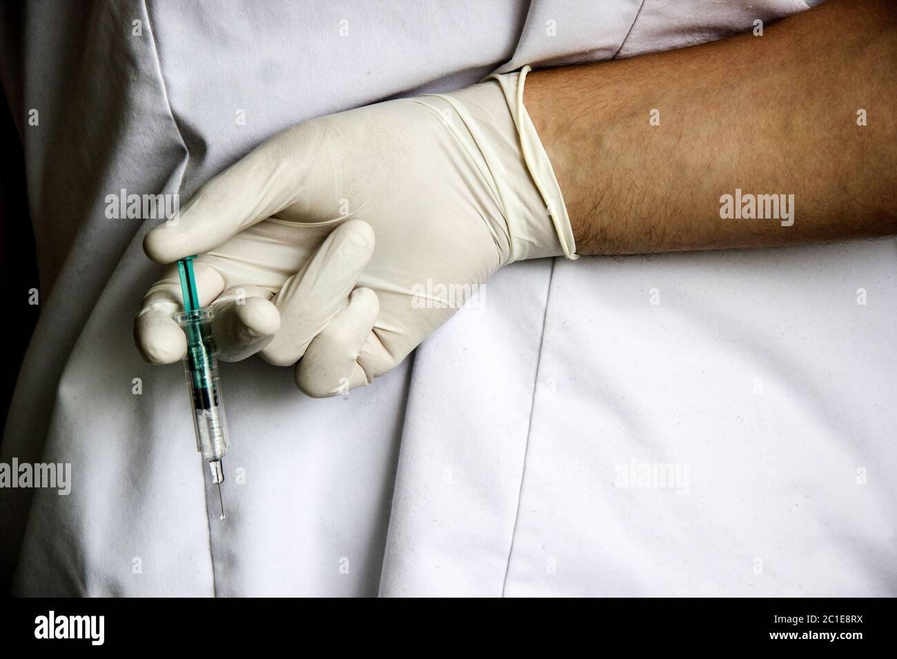 Doctor hand in white glove hold syringe with preparation jet from the needle. Medical man holding injector with drugs in arm. Su Stock Photo