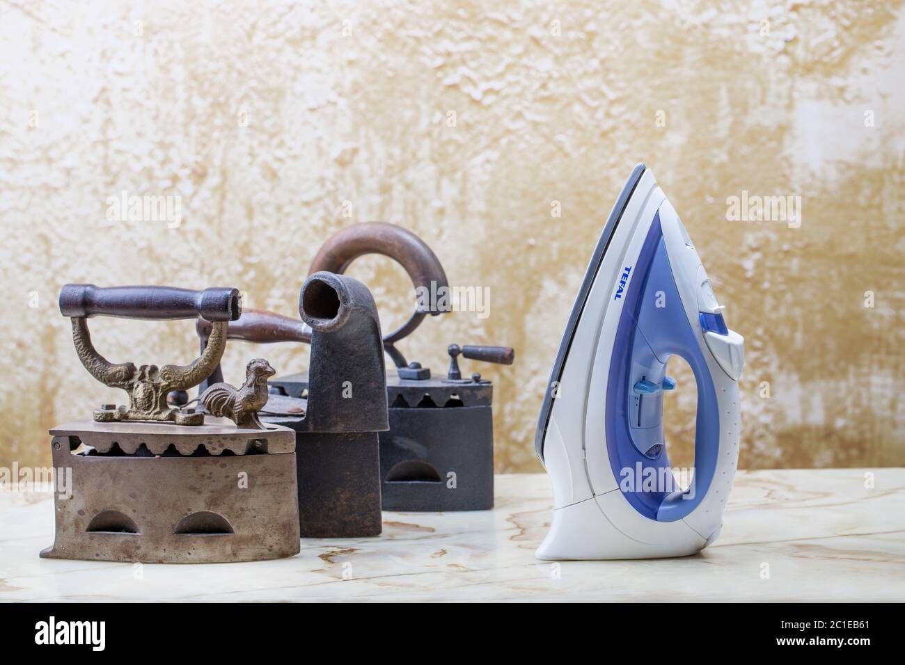 Cocept of old and new technologies. Photo of old and modern irons on the vintage stucco background. Stock Photo