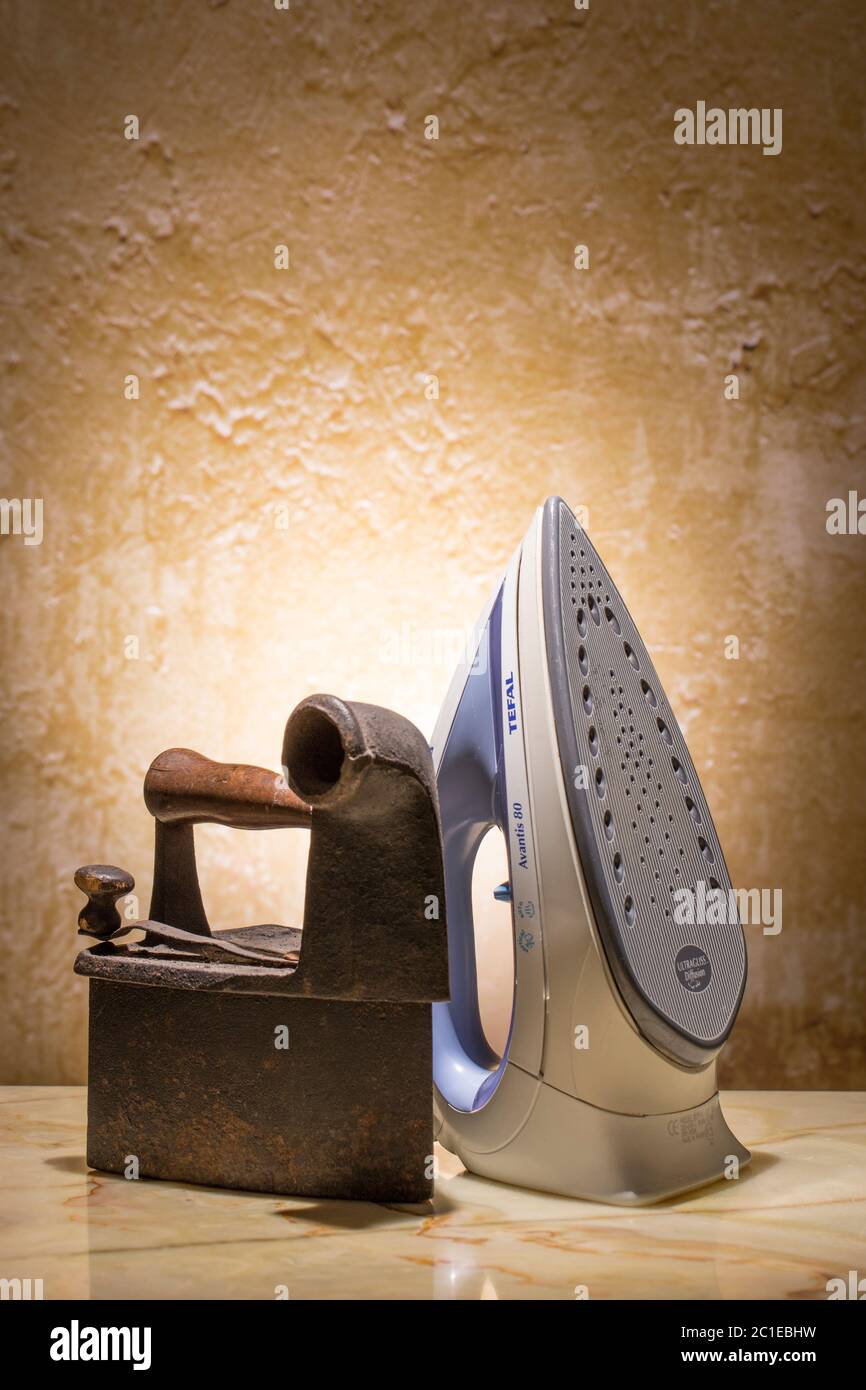 Cocept of old and new technologies. Photo of old and modern irons on the vintage stucco background. Stock Photo