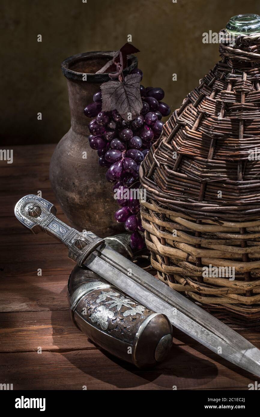 Beautiful example of caucasian dagger with willow-vine-bound bottle, silver powder flask and clay jug on wood background. 19th century (Time of Russia Stock Photo