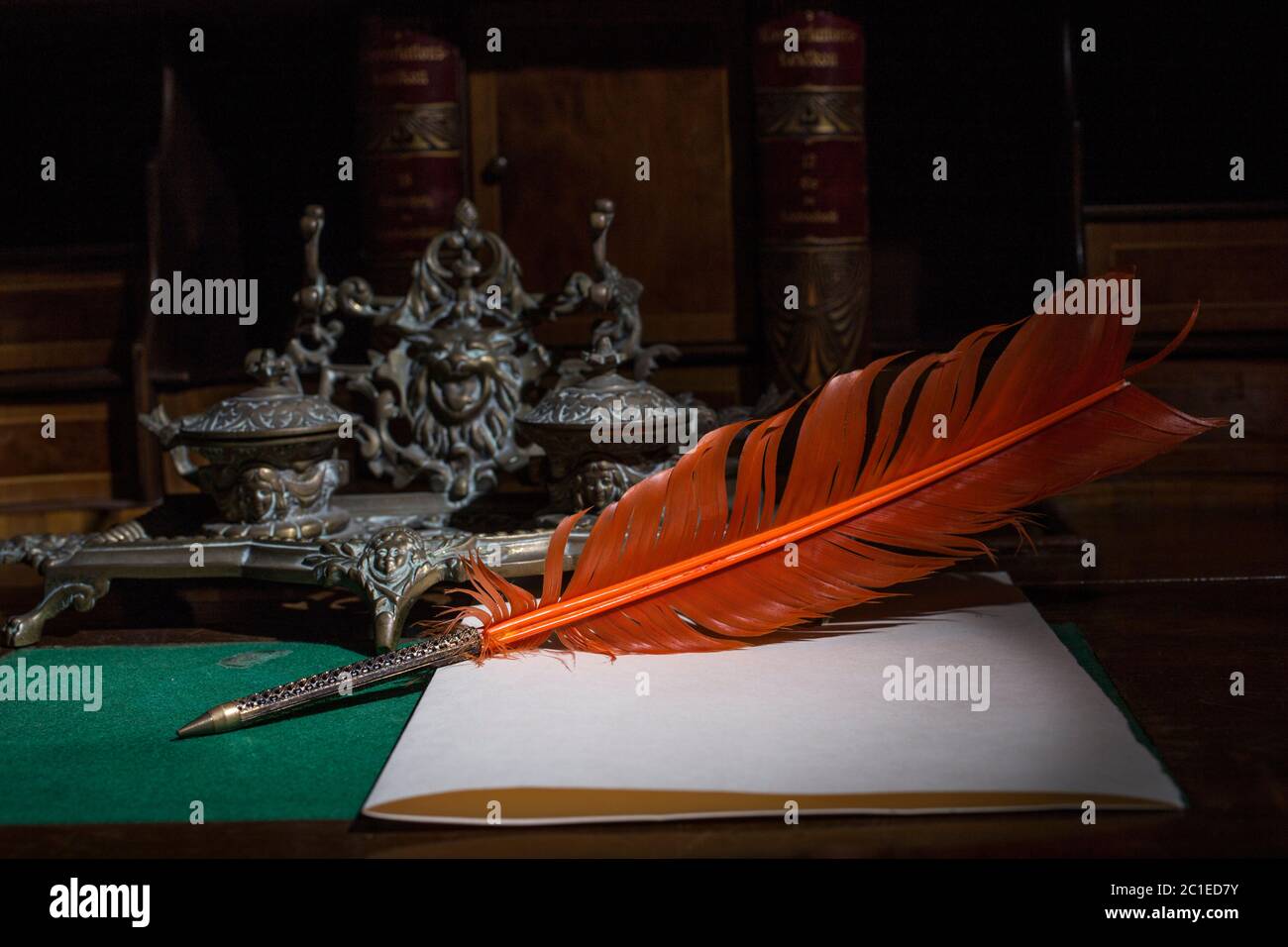 Retro quill pen and vintage inkwell on wooden desk in the old office against the background of the bookcase and the rays of light. Conceptual backgrou Stock Photo