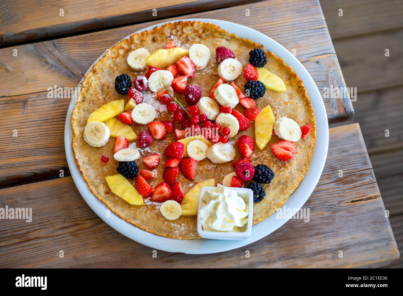 Large pancake with summer fruit and whipped cream on a wooden table. Top view. Stock Photo