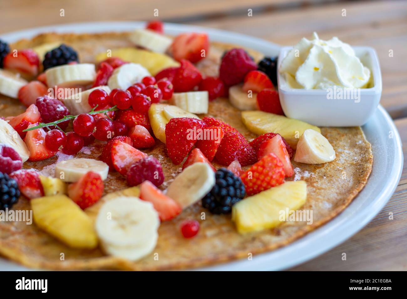 Large pancake with summer fruit and whipped cream on a wooden table. Close up Stock Photo