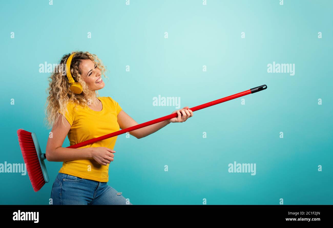 Girl with headset use the broom like a guitar. Cyan background Stock Photo