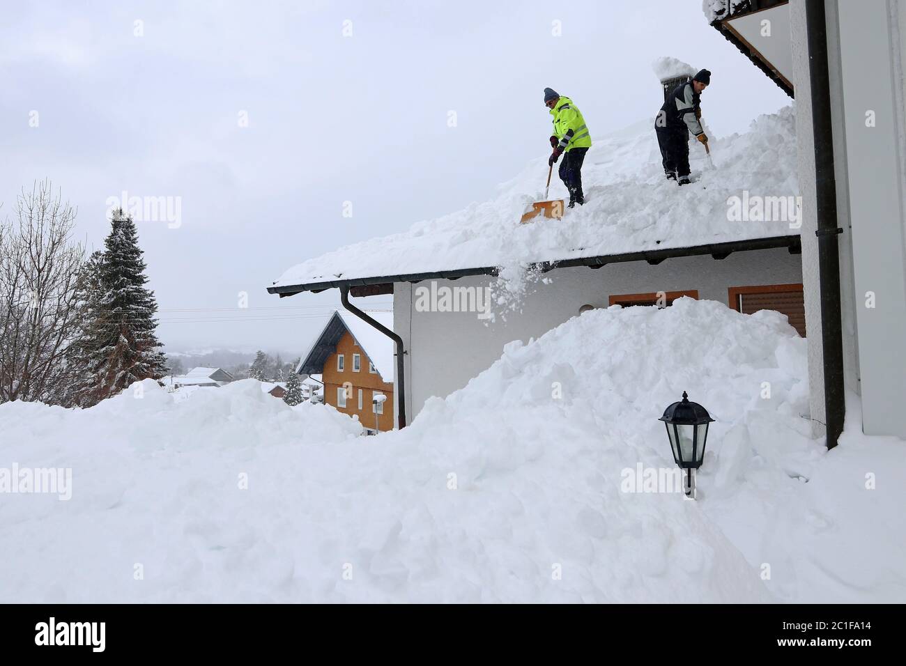 Two men shoveling high, heavy snow from a house roof Stock Photo