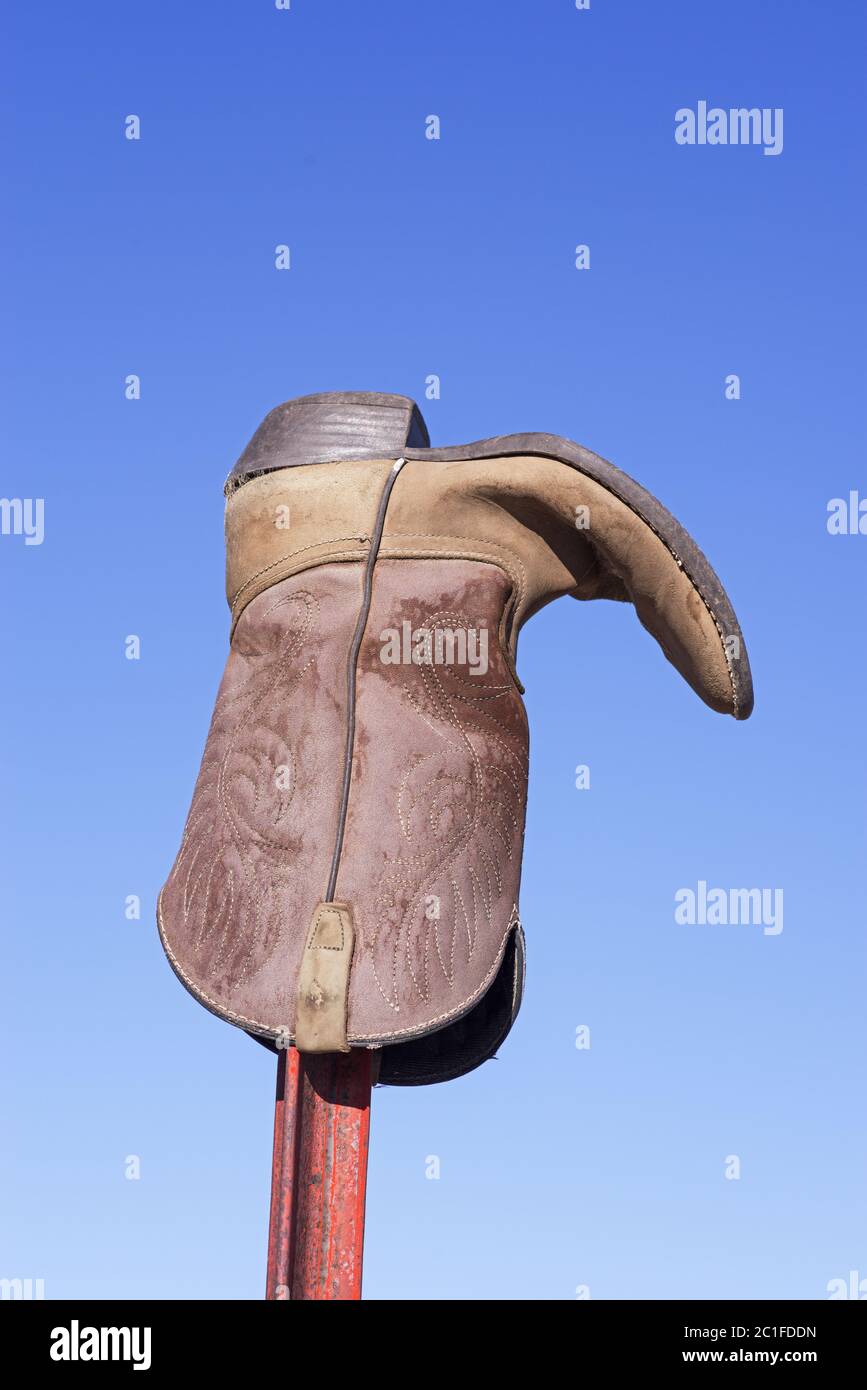 an old weathered cowboy boot on a metal fence post with blue sky background Stock Photo