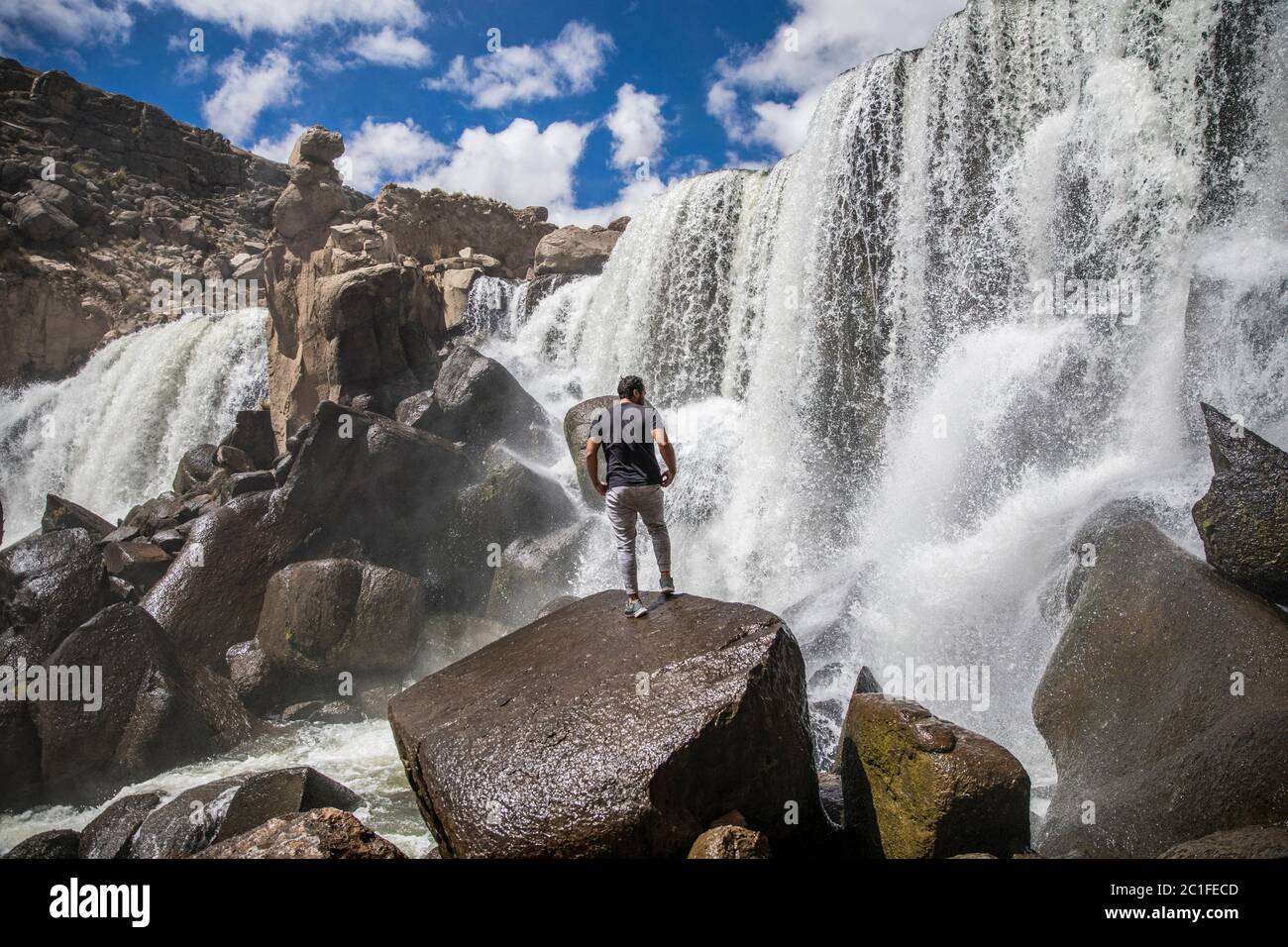 man standing on a rock near a big waterfall, clouds and blue sky Stock Photo