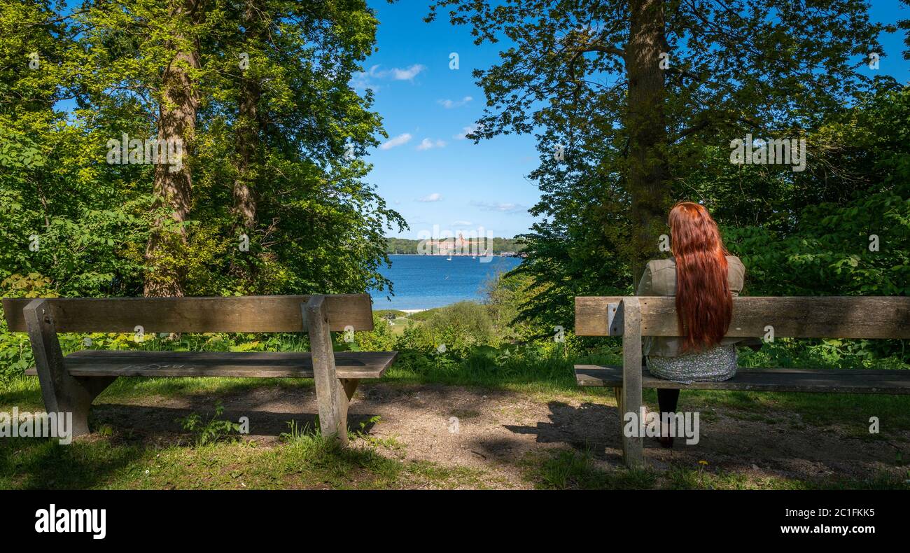 Woman with red hair sitting lonely on a bank in a park Stock Photo