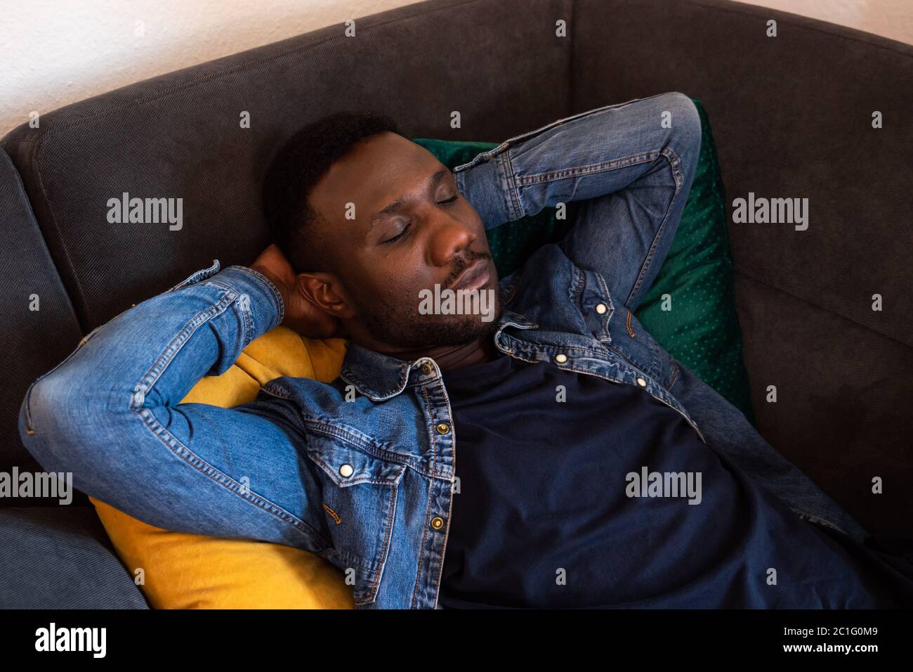 Young black man napping on couch with hands behind head. Medium shot. High angle. Stock Photo
