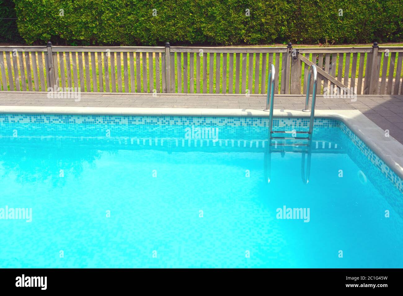Modern swimming pool with pool cover for protection dirt rolled up and pool ladder in garden