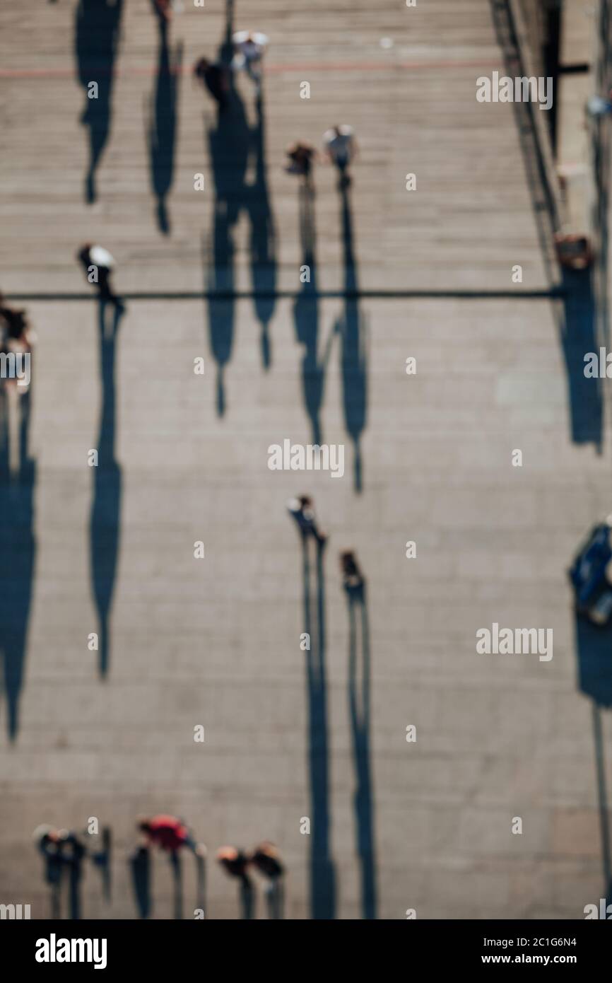 Overhead view of blurred pedestrians walking below, casting long shadows Stock Photo
