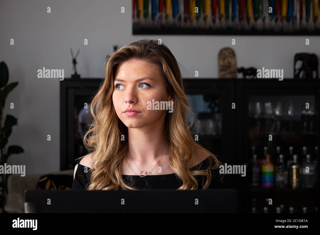 Young blond woman looking away thinking in living room. Medium shot. Stock Photo