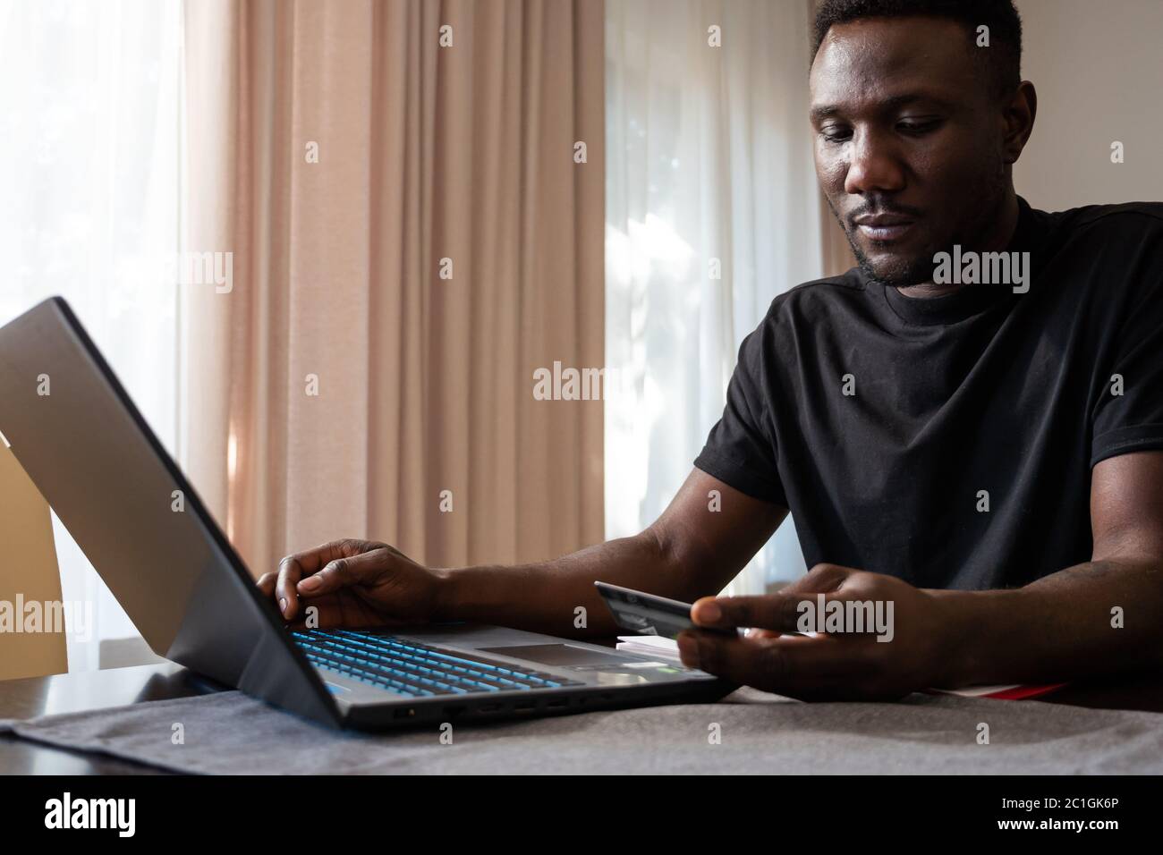 Young black man shopping online holding credit card at home in front of laptop. Medium shot. Stock Photo
