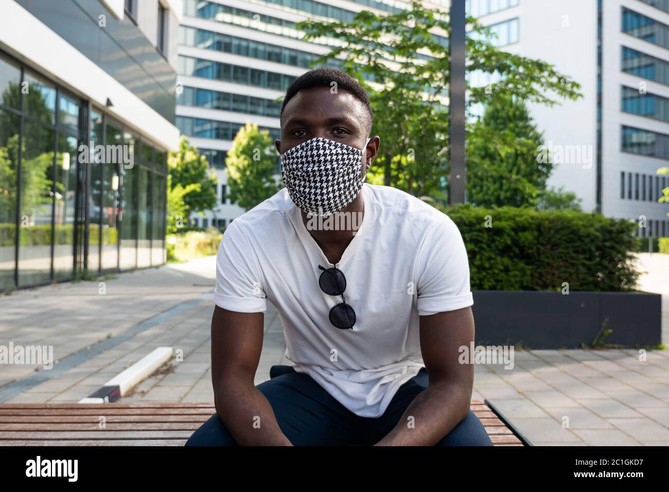 Young black man wearing face mask looking at camera. Medium shot. Outdoors. City Background. Stock Photo