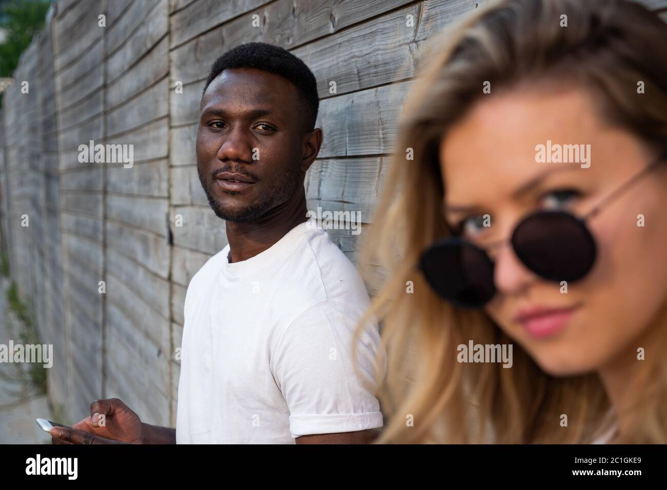 Young black man looking at camera. White woman in foreground. Focus on background. Stock Photo