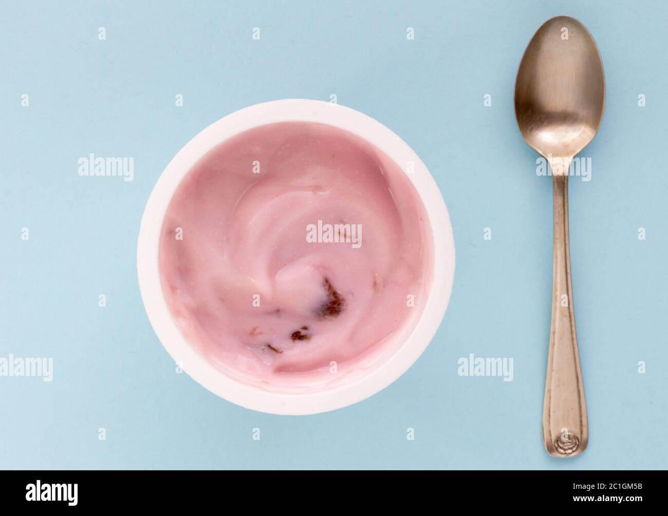 Yogurt in plastic cup close up with small silver spoon, top view photo