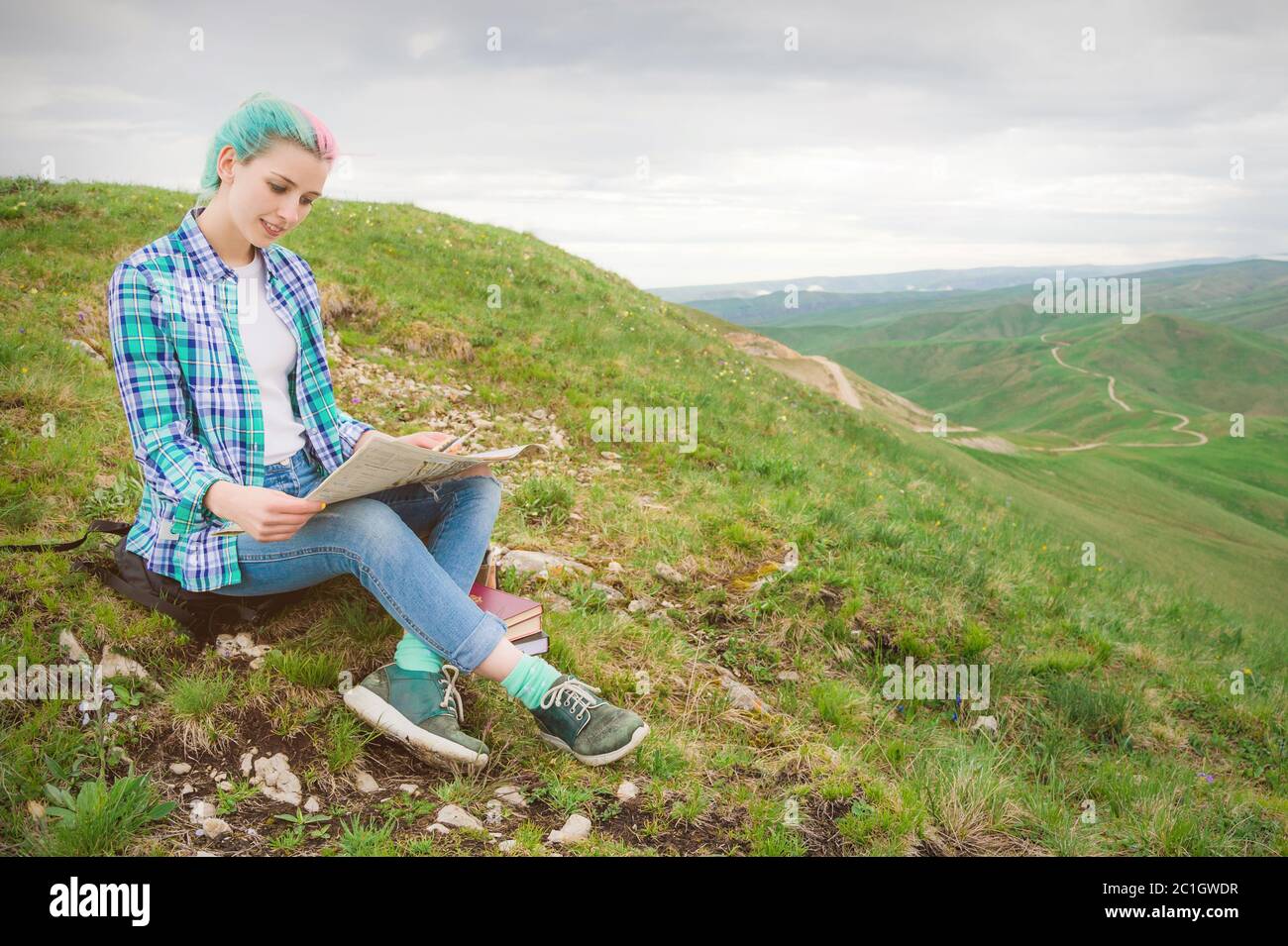 Girl traveler with multi-colored hair sitting on nature reading card and holding a compass in hand. The concept of navigating th Stock Photo