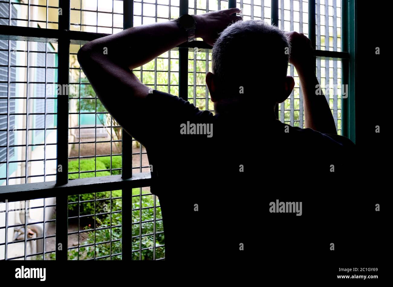 silhouette man leaning against a window bars. Prisoner concept Stock Photo