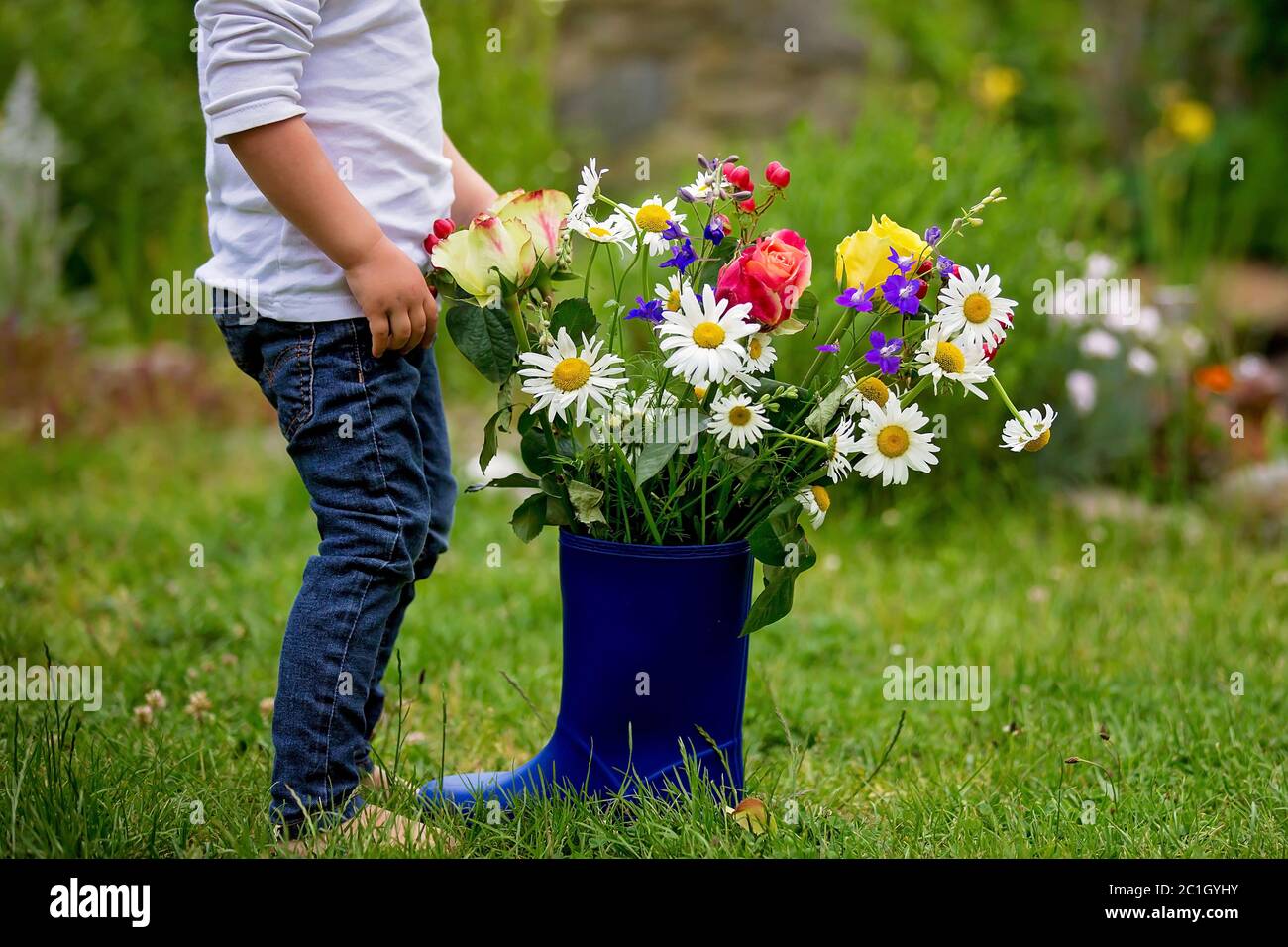 Child holding rubber boots with beautiful flowers in garden Stock Photo