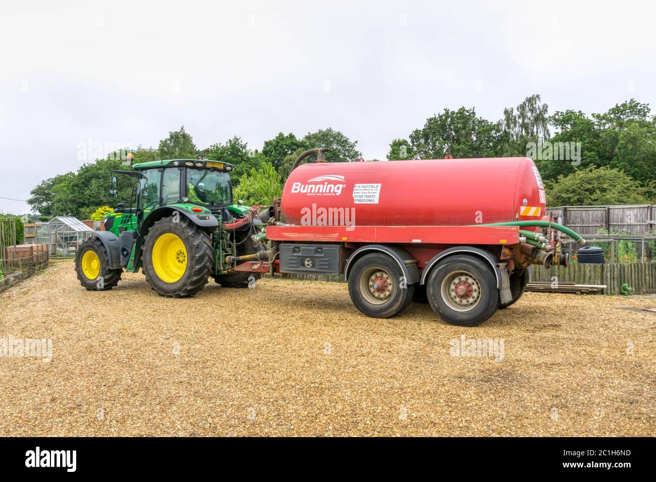 A John Deere 6120R tractor with a tanker at a house in the country, to empty the septic tank. Stock Photo