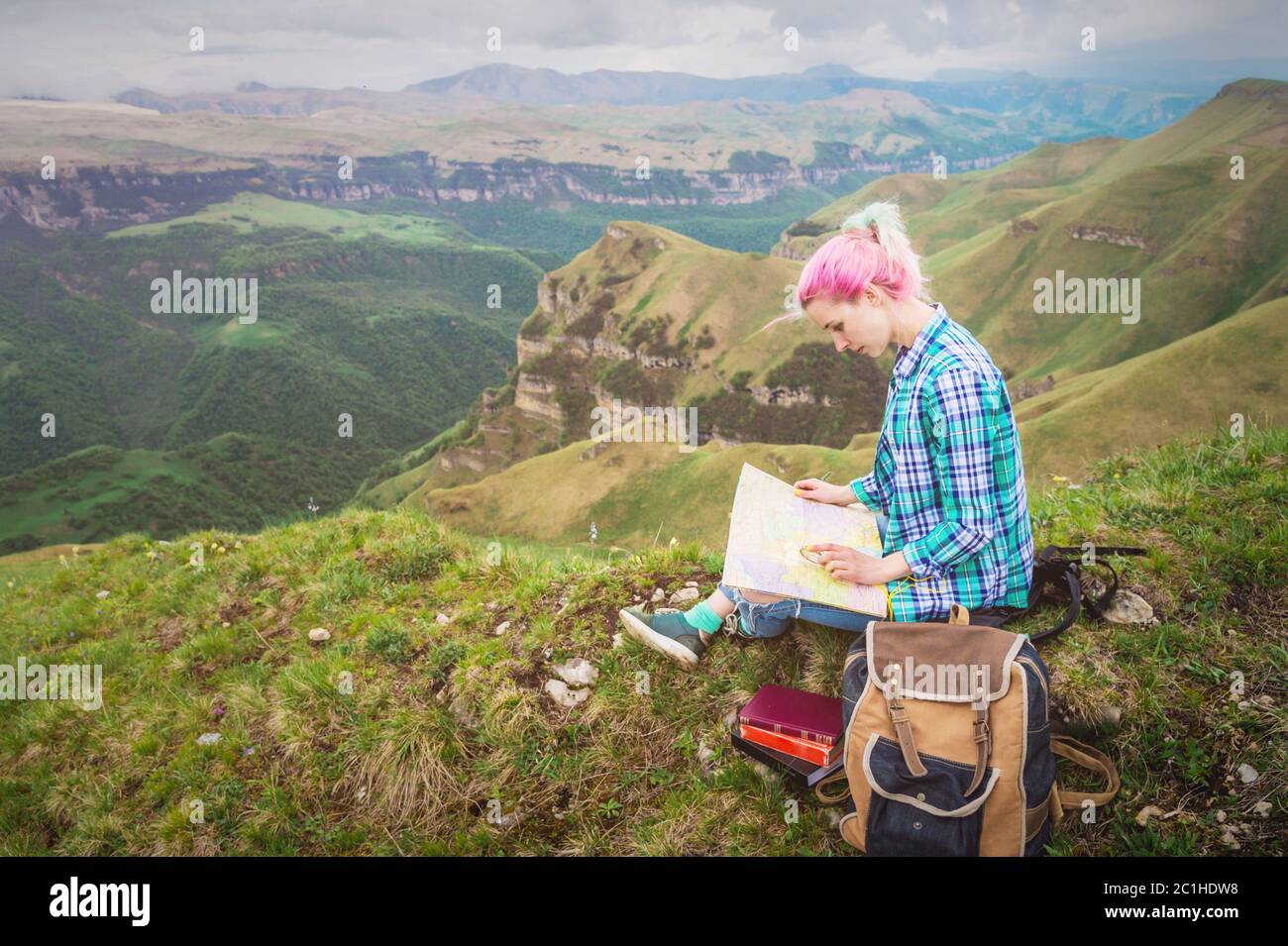 Girl traveler with multi-colored hair sitting on nature reading card and holding a compass in hand. The concept of navigating th Stock Photo