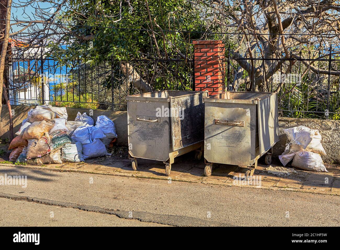 A pile of garbage bags stacked near steel trash cans on the side of a