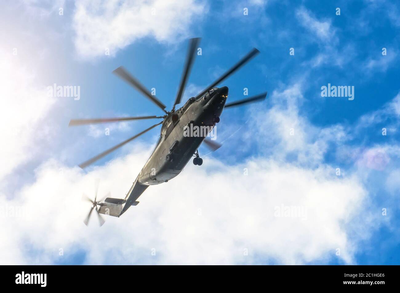 A large transport helicopter is gaining height in the sky clouds of sun