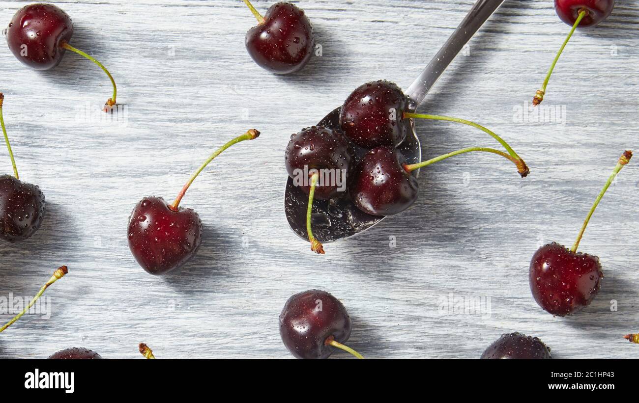 The spoon with juicy ripe cherries in water droplets with berries on a gray wooden background. Stock Photo