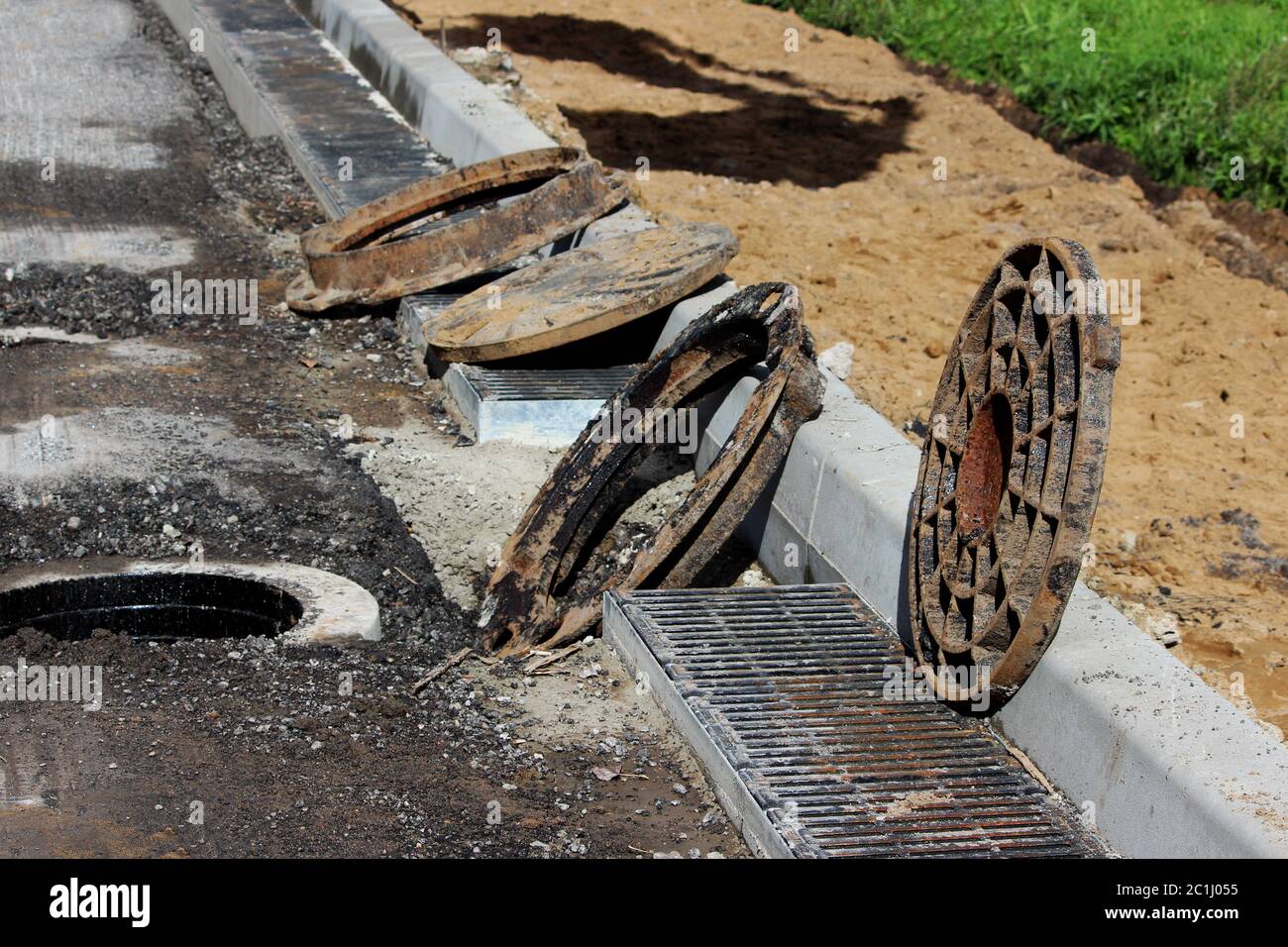 many rusty round hatches and a rainwater grid on the side of the city road. repair and expansion of the road at the exit of the Stock Photo