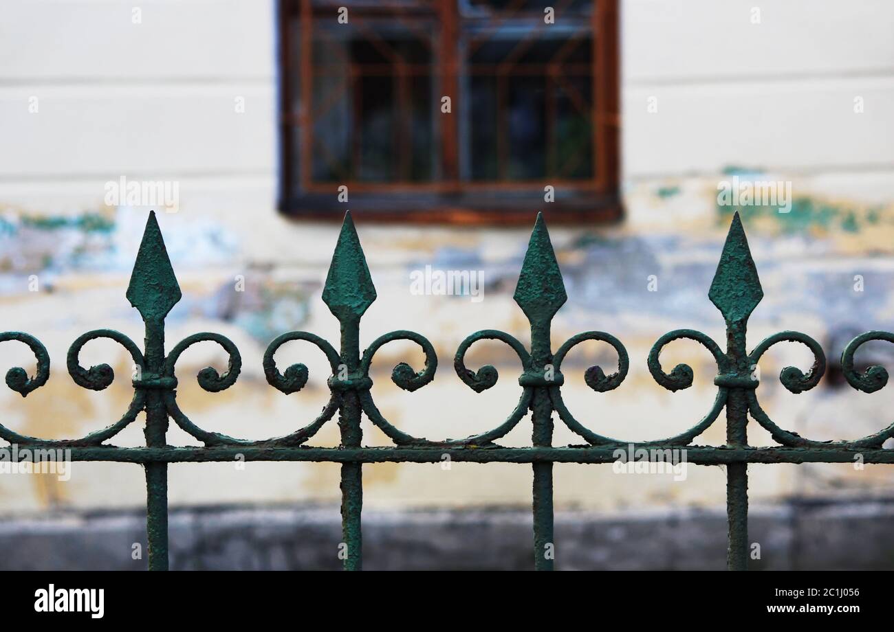 The old metal city fence with sharp points is painted on top with green paint, which is flaky Stock Photo
