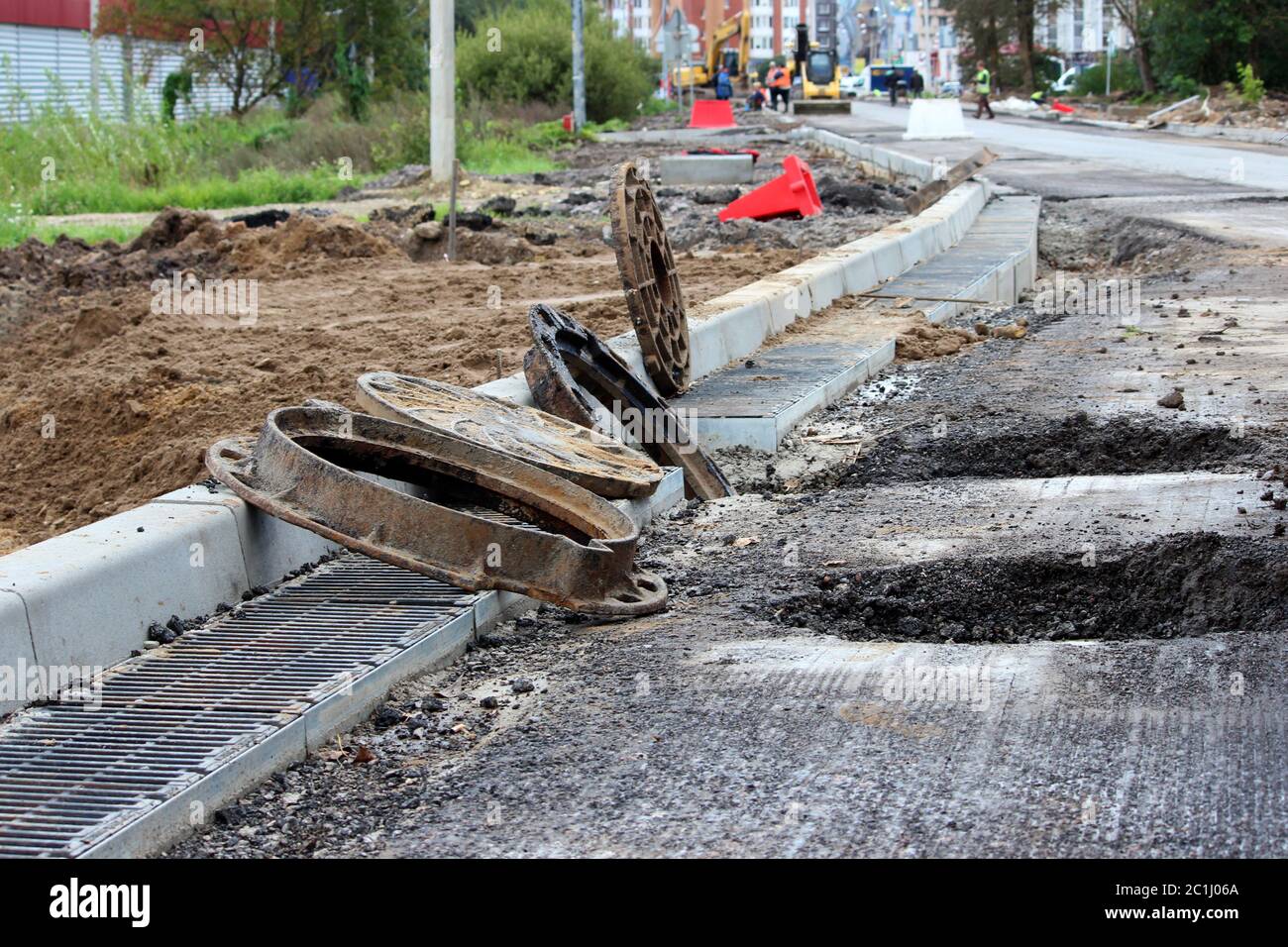 many rusty round hatches and a rainwater grid on the side of the city road. repair and expansion of the road at the exit of the Stock Photo