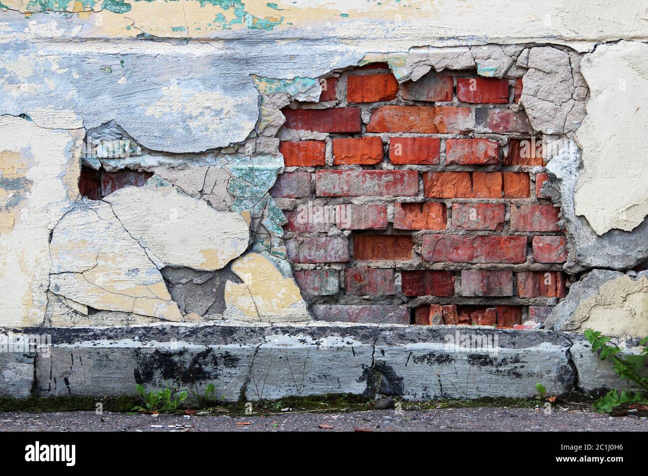 An old wall with peeling beige plaster under which red brickwork is visible Stock Photo