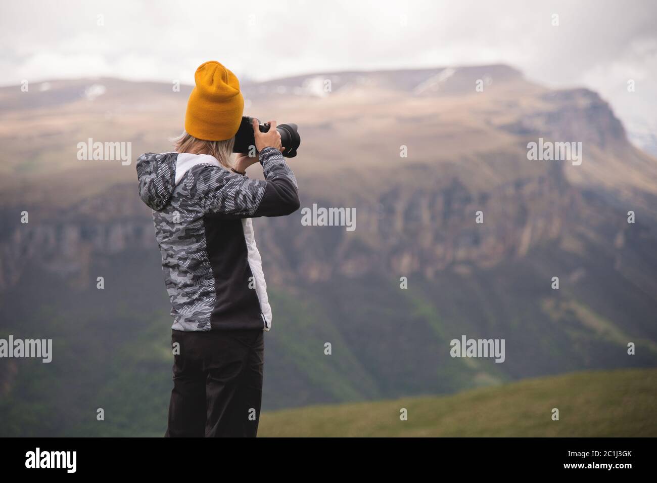 A young girl takes pictures of a plateau on top of a high mountain on a cloudy day. View of the girl behind Stock Photo
