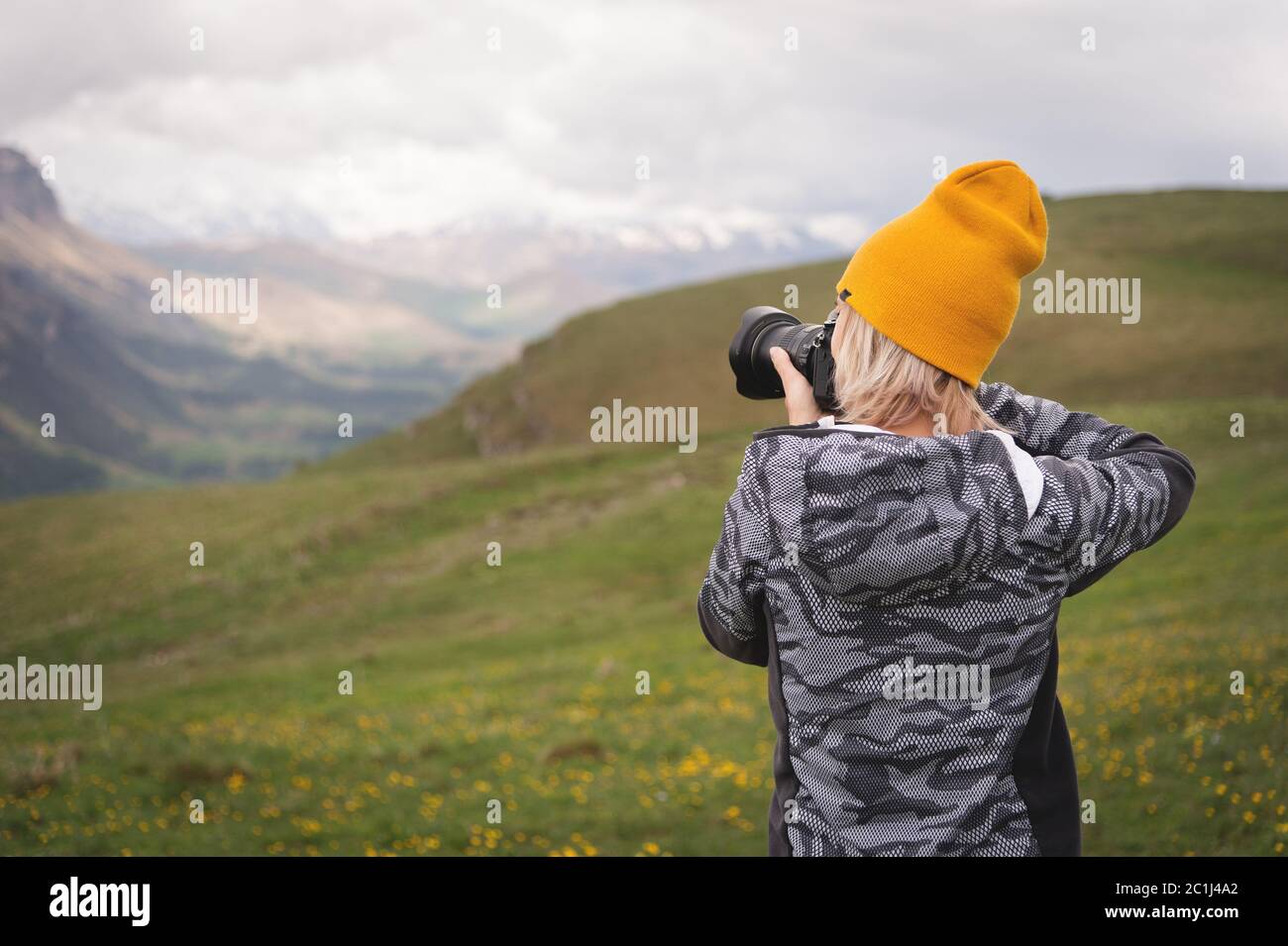 A young girl takes pictures of a plateau on top of a high mountain on a cloudy day. View of the girl behind Stock Photo