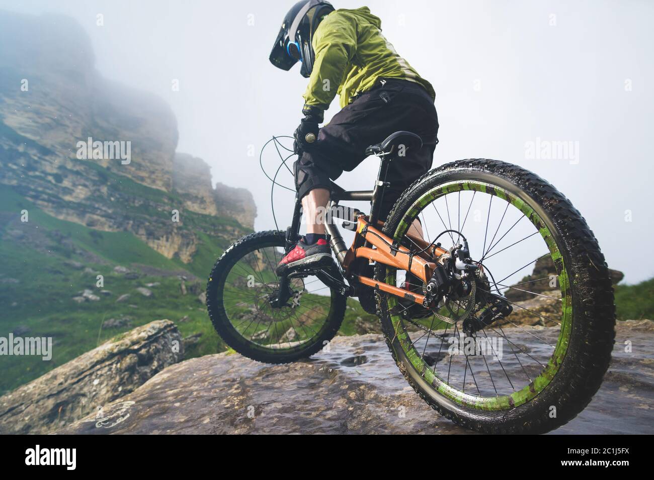 Legs of bicyclist and rear wheel close-up view of back mtb bike in mountains against background of rocks in foggy weather. The c Stock Photo
