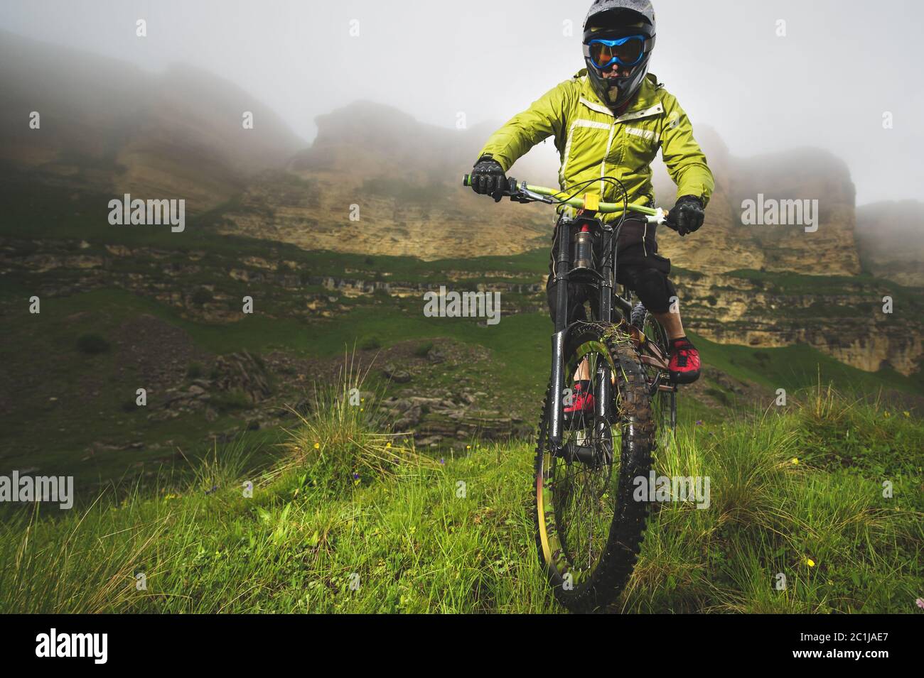A man in a mountain helmet riding a mountain bike rides around the beautiful nature in cloudy weather. downhill Stock Photo