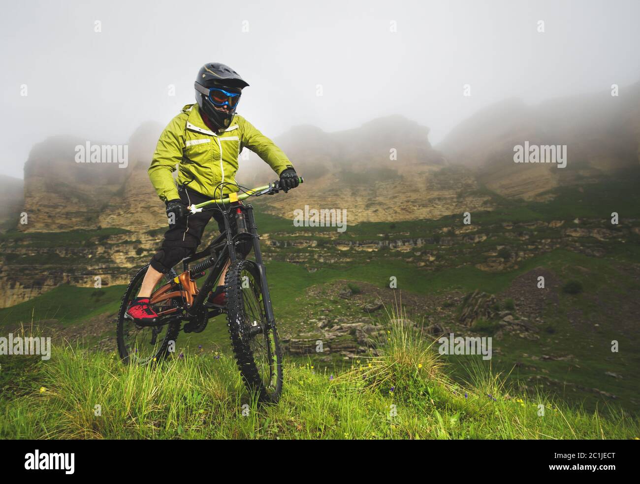A man in a mountain helmet riding a mountain bike rides around the beautiful nature in cloudy weather. downhill Stock Photo