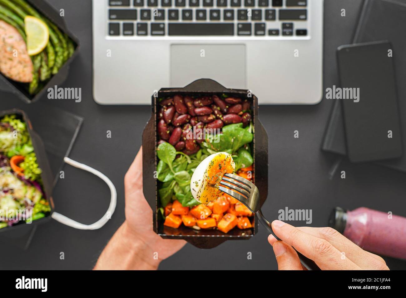 Male hands holding food delivery box eating lunch at work in office, flat lay. Stock Photo