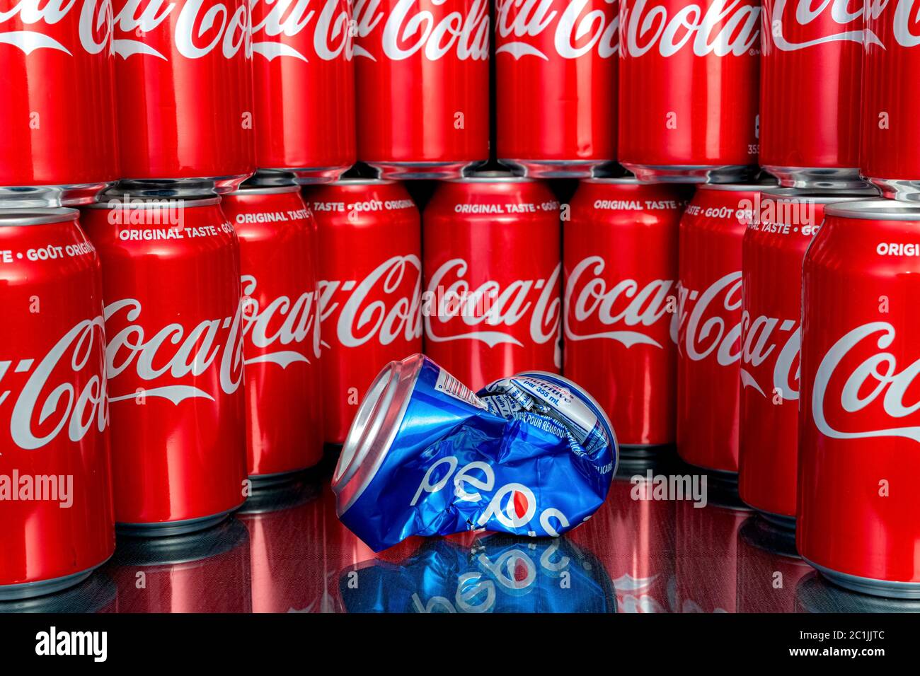 Saint John, NB, Canada - April 28, 2020: Many cans of Coca Cola surround a crushed Pepsi can. Shallow depth of field, focus on Pepsi can. Stock Photo